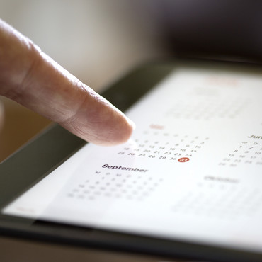 Ein Finger, der auf das Display von einem Tablett tippt auf dem ein Kalender zu sehen ist.
